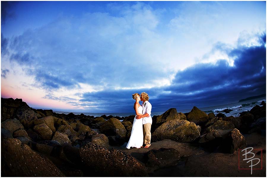 Bride and groom under dramatic light at the beach