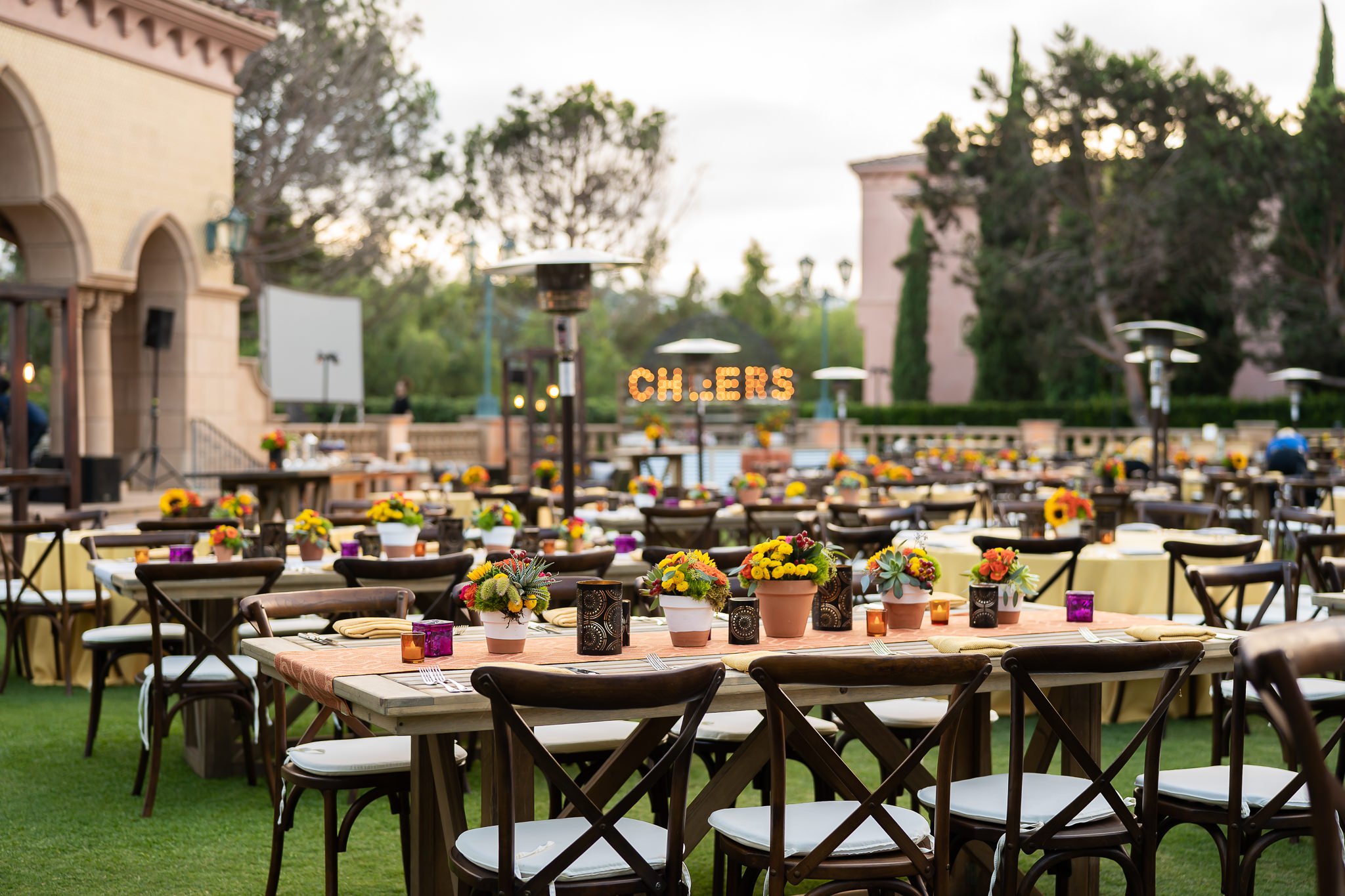 An elegant outdoor event setup with wooden tables and chairs arranged on a lush green lawn