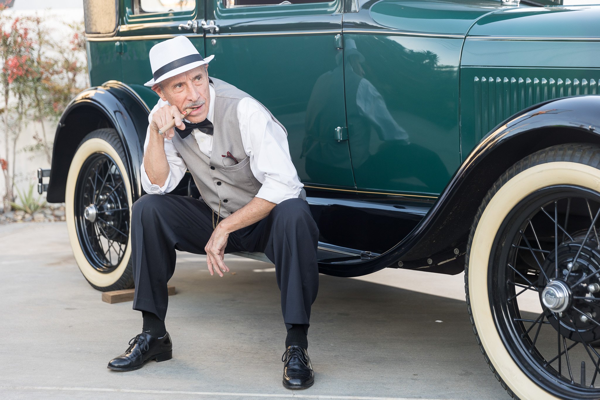 A man in a hat and suit sits on a vintage car