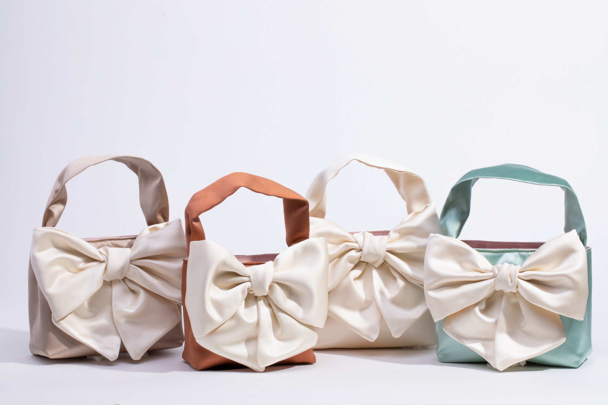 Four purses in different colors, each adorned with a decorative bow