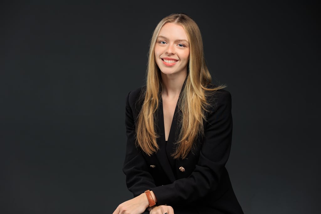 A woman in a black suit sits confidently on a chair