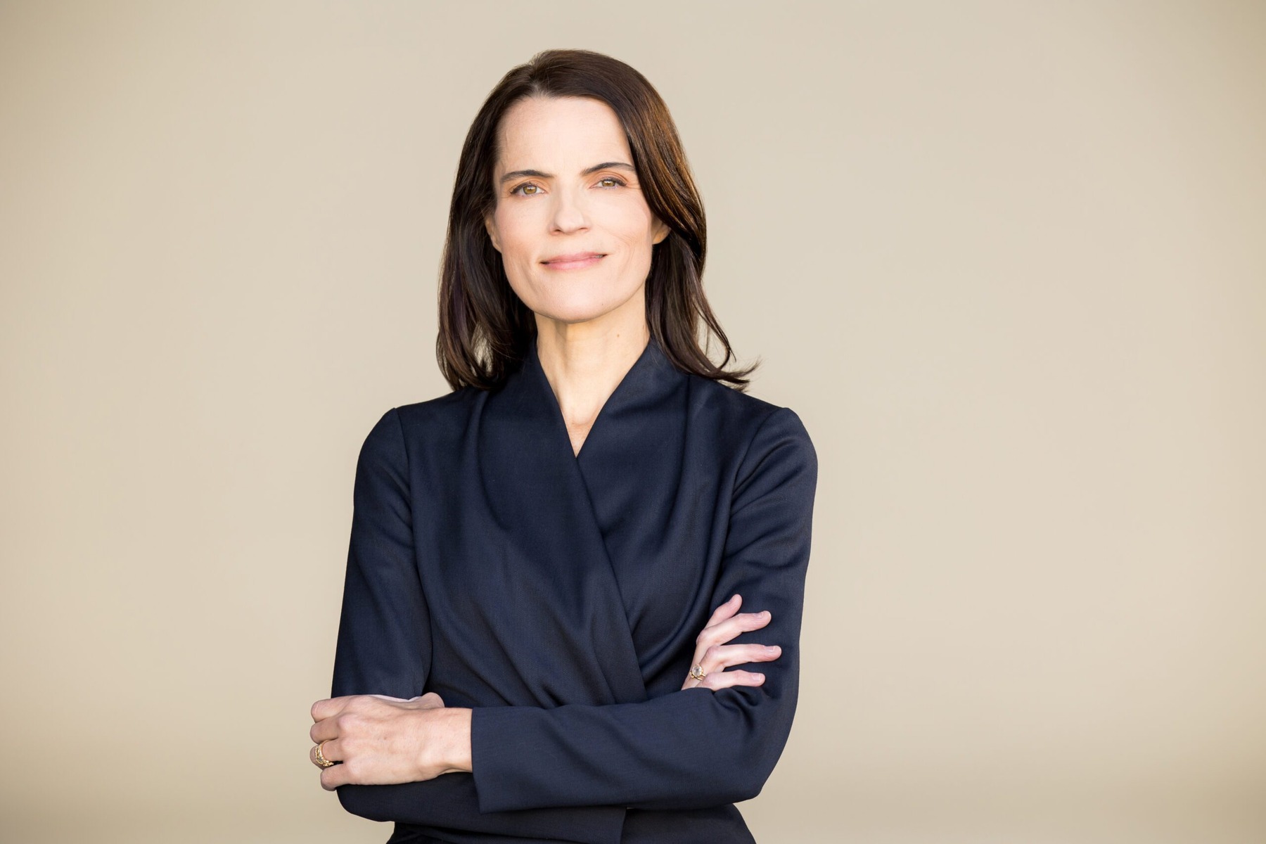 A confident woman in a navy suit with crossed arms smiles against a neutral background