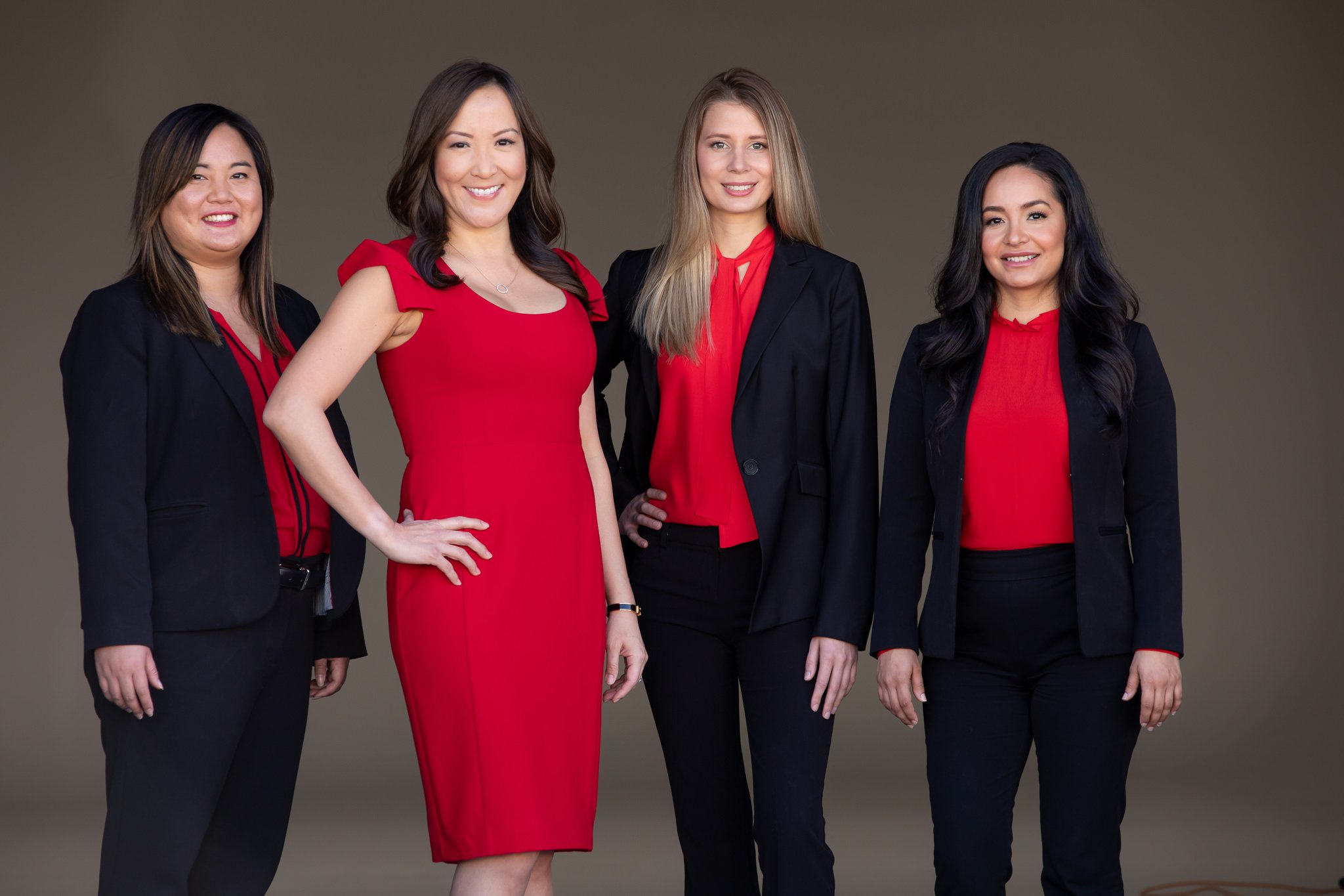 Four businesswomen in black suits and red tops posing together