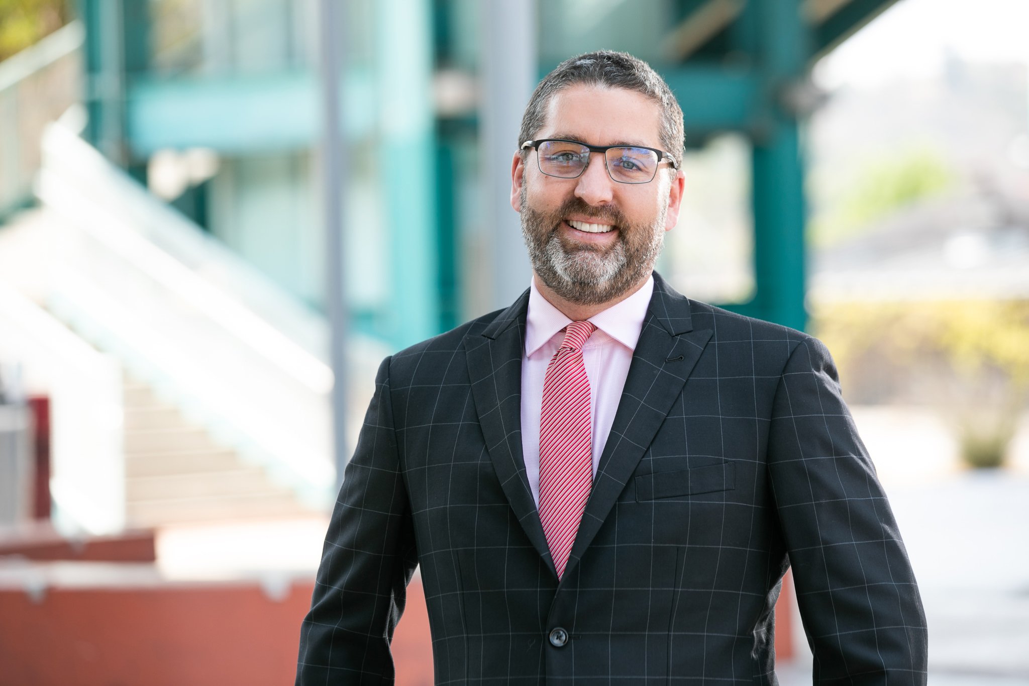 Smiling businessman in glasses and suit standing outside an office building