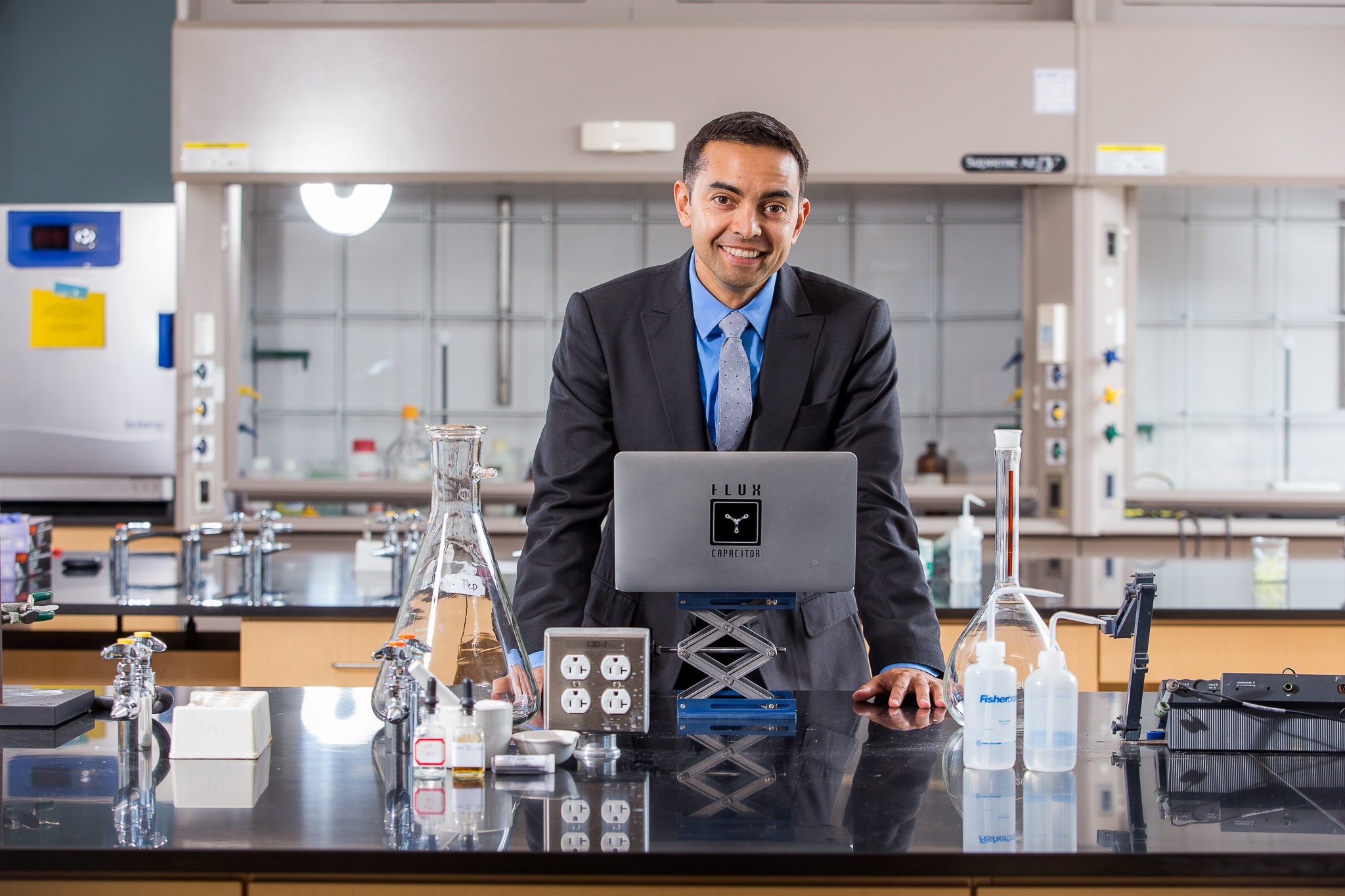 Man in a suit smiling behind a laptop in a science lab