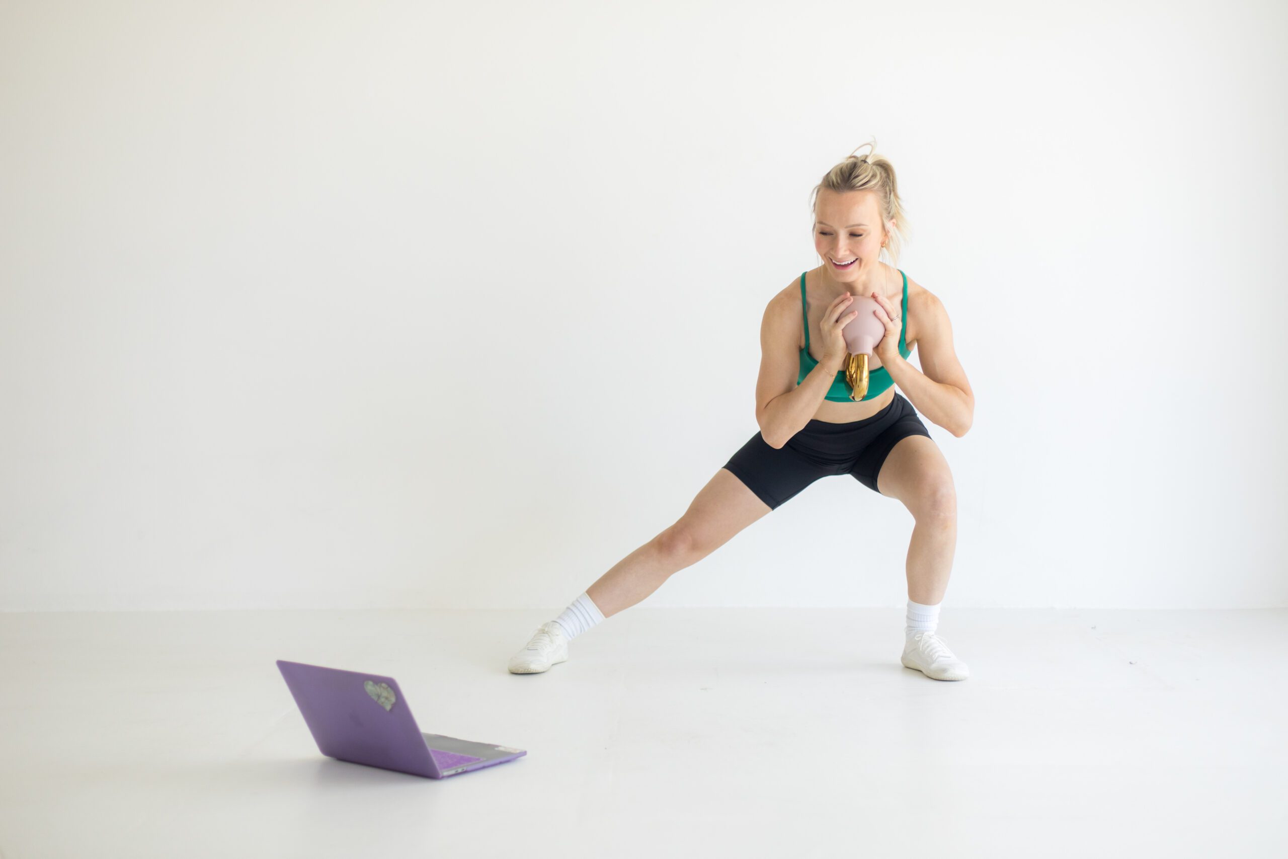 Fitness trainer doing a kettlebell workout beside a laptop
